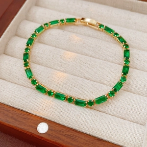 Detail of gold-plated bracelet with emerald green zircons on beige linen cushion