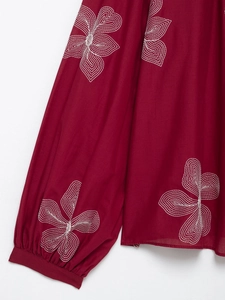 Detail of dark red blouse featuring white floral embroidery and elastic sleeve cuffs