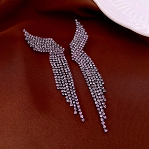 Detailed macro view of purple rhinestone wing tassel earrings on a brown silk background