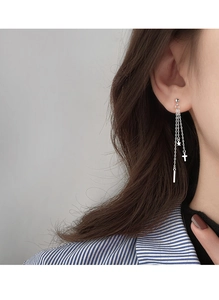 Close-up of silver tassel earrings with cross and star pendants worn by a woman