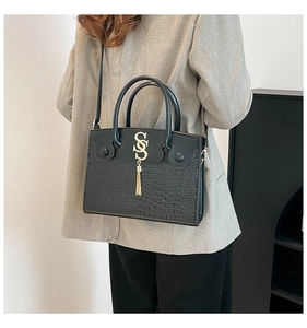 Detail of black tote bag featuring crocodile pattern leather and gold fringe ornament