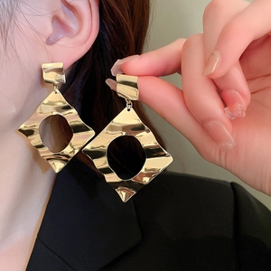 Detail of oversized gold geometric earrings with hammered texture on a model