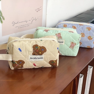 Three quilted bear cosmetic bags in beige, green, and blue on a wooden surface