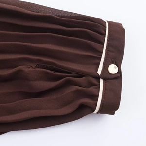 Close-up of pleated dark brown midi dress sleeve with white piping and gold button