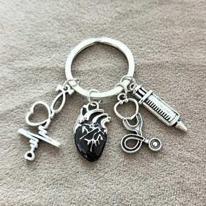 Detail of medical keychain with syringe, stethoscope, and heart pendants on grey texture