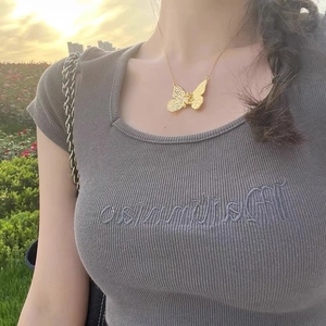 Textured gold butterfly pendant necklace worn by a model in soft outdoor lighting