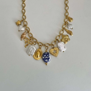 Detail of gold multi-charm necklace featuring baroque pearl, shell, and blue ceramic bead