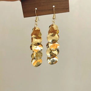 Détail de longues boucles d'oreilles dorées à paillettes avec disques sur bloc en bois