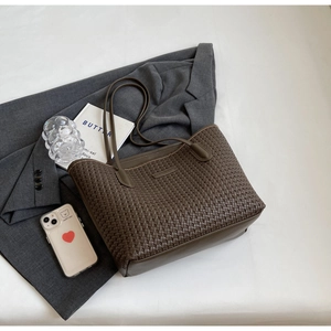 Detail of dark brown woven tote bag on grey blazer for a modern lifestyle aesthetic