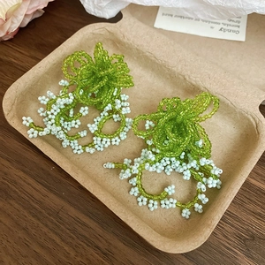 Detail of handmade green and white beaded floral tassel earrings on rustic tray