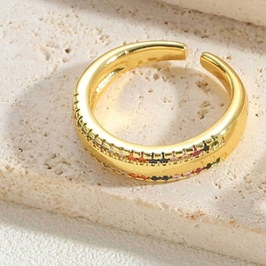 Close-up of gold crescent ring with colorful inlaid stones on beige stone surface