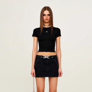 Détail de la mini-jupe en jean noir avec des rivets métalliques et boucle de ceinture en X