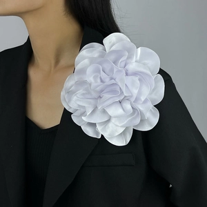 Detail of a large 19cm white satin floral brooch pinned on a black suit shoulder
