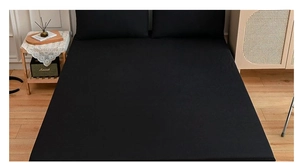 Close-up of matte black bedding set with fitted sheet and pillowcases on a wooden floor