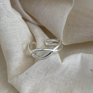 Minimalist 925 sterling silver crossover ring with adjustable open design on linen