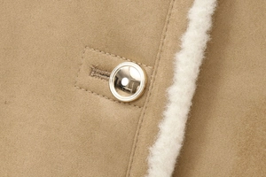 Detail der kamelfarbenen Wildlederjacke mit goldenen Metallknöpfen und weißem Fleece-Futter