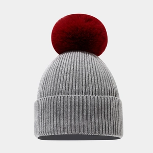 Detail of grey ribbed knit beanie with a large crimson faux fur pompom for winter