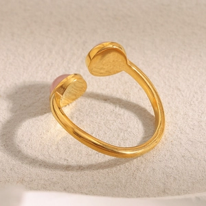 Bague ouverte en acier doré 18K avec pierres d'agate rose sur un fond gris épuré