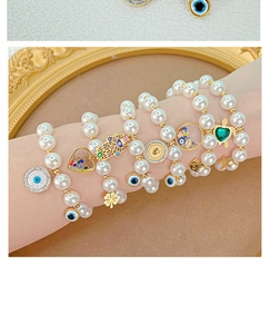Detail of layered gold-tone bracelets with pearl beads and symbolic charms on wrist