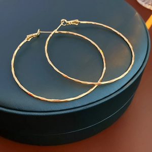 Macro shot of gold hoop earrings with faceted texture on a dark green jewelry box