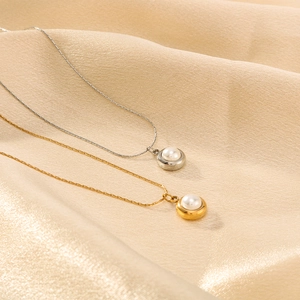 Gold and silver titanium necklaces with pearl circle pendants on beige silk fabric