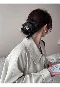Detail of a black denim scrunchie with beige label worn on a high bun hairstyle