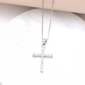 Silver cross pendant necklace with cubic zirconia on white marble surface