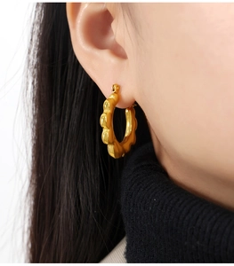 Detailed view of textured gold sunflower-shaped hoop earrings on a fashion model