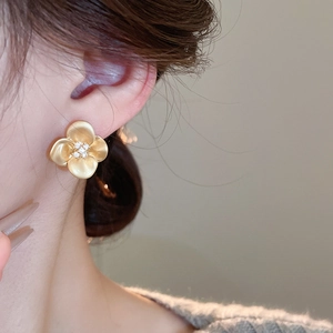 Close-up of elegant gold flower earrings with a crystal center on model's ear