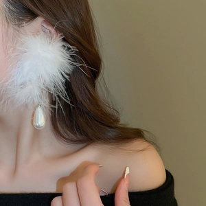 Detailed view of oversized earrings featuring white feathers and drop-shaped pearls