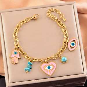 Gold-tone charm bracelet with pink evil eye and hamsa hand pendants in a gift box