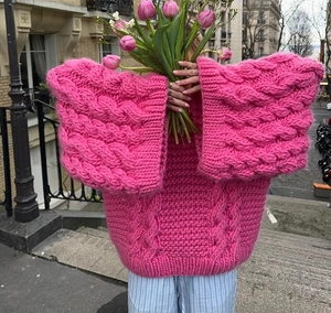 Close-up of chunky knit fuchsia sweater with wide flare sleeves and cable texture