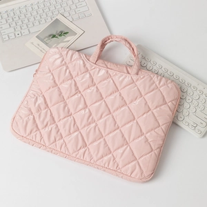 Pink quilted puffer laptop sleeve bag with reinforced handles on a minimalist desk