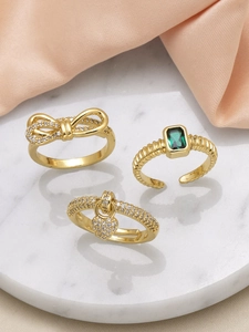 Detailed view of three gold-plated rings with zircon bow and emerald heart on marble