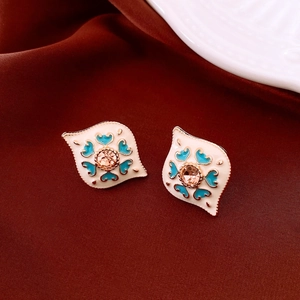 Detailed close-up of vintage enamel stud earrings with pink gemstone on red silk fabric