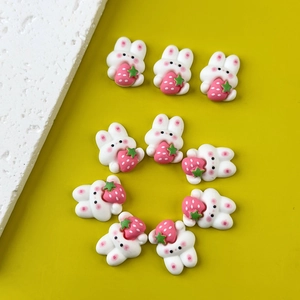 Flat lay of ten cute white resin bunnies holding pink strawberries for DIY crafts