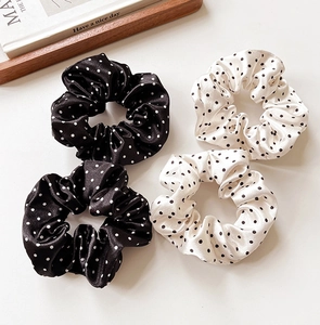 Close-up of four satin polka dot scrunchies in black and beige on a wooden tray