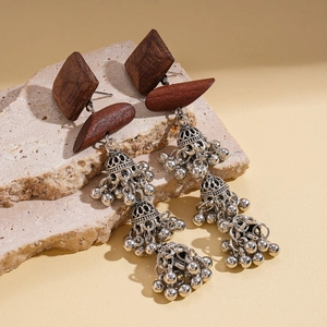 Detail of bohemian wood earrings with silver metallic bells on a textured stone surface