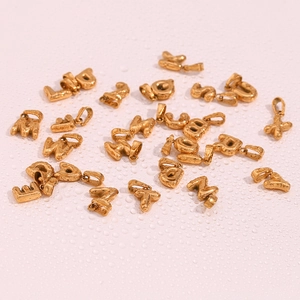 Close-up of mini gold bubble letter pendants on pink surface with water drops