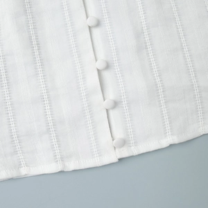 Macro detail of textured white cotton fabric with covered buttons and V-neck lace trim