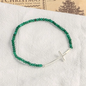 Natural green stone beaded bracelet featuring a silver cross pendant on a linen surface