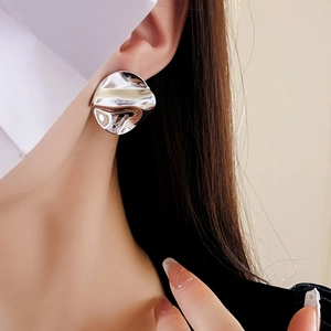 Close-up of asymmetric silver textured earrings worn by a model in soft lighting