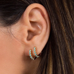 Close-up of model wearing two golden turquoise earrings in a s925 silver setting