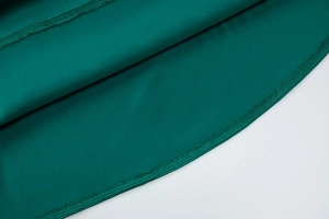 Détail de la couture et texture du tissu satiné vert émeraude sur l'ourlet de la jupe