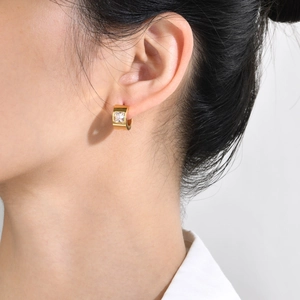 Close-up of a gold hoop earring with square zircon worn by a model in soft lighting