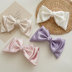 Close-up of four satin bow hair clips in beige white pink and purple colors