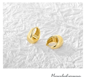 Macro detail of high-polish gold-plated C-shaped hoop earrings on textured background