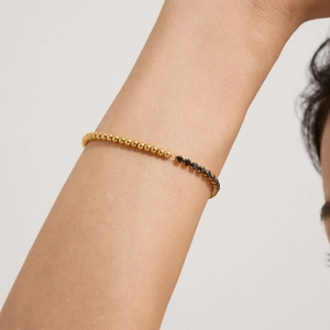 Detail eines eleganten zweifarbigen Armbands mit Goldperlen und schwarzen Steinen am Handgelenk
