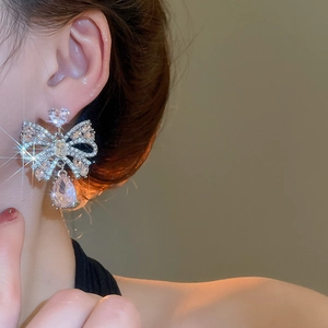 Close-up of sparkling bow knot earrings with water drop crystals on a model's ear