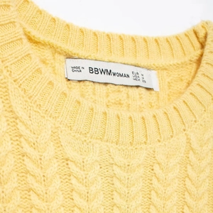Detail of a yellow short-sleeve knit top with ribbed round neck and BBWM brand label